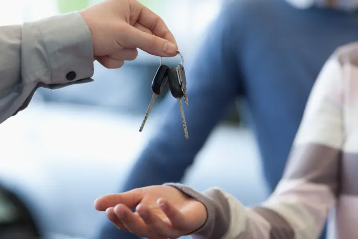 Fahrzeugschlüssel werden bei der Übergabe eines Autos in eine offene Hand gereicht